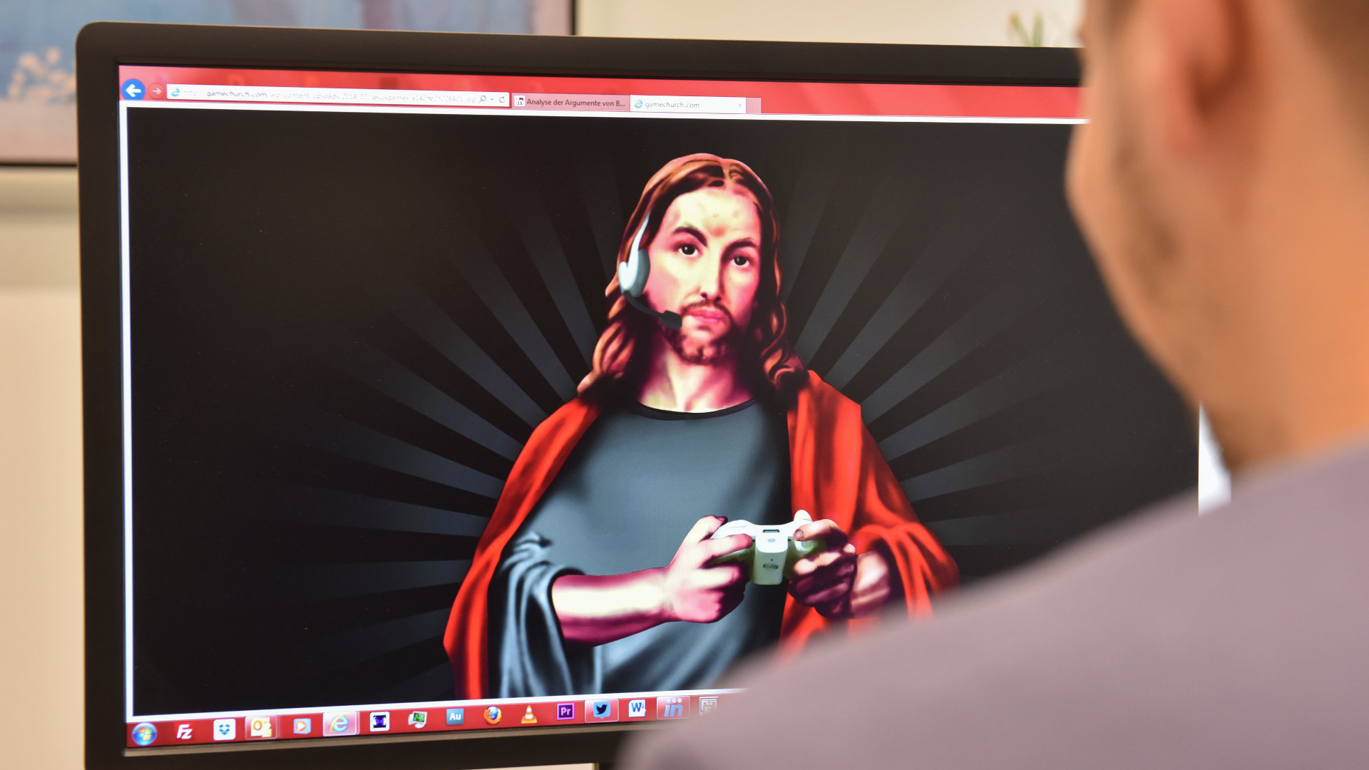 Ein Mann sitzt vor einem Computerbildschirm. Er schaut auf das Logo von "Gamechurch": ein Bild von Jesus mit Spielecontroller und Headset.