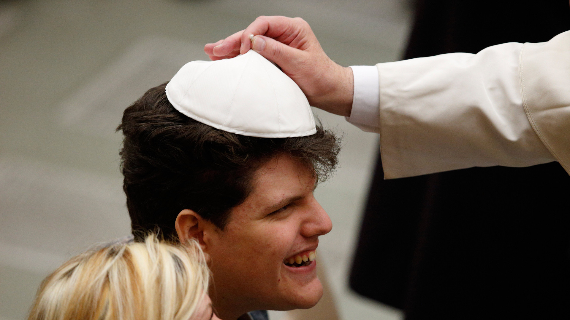 Papst Franziskus setzt einem Jungen sein Pileolus auf.
