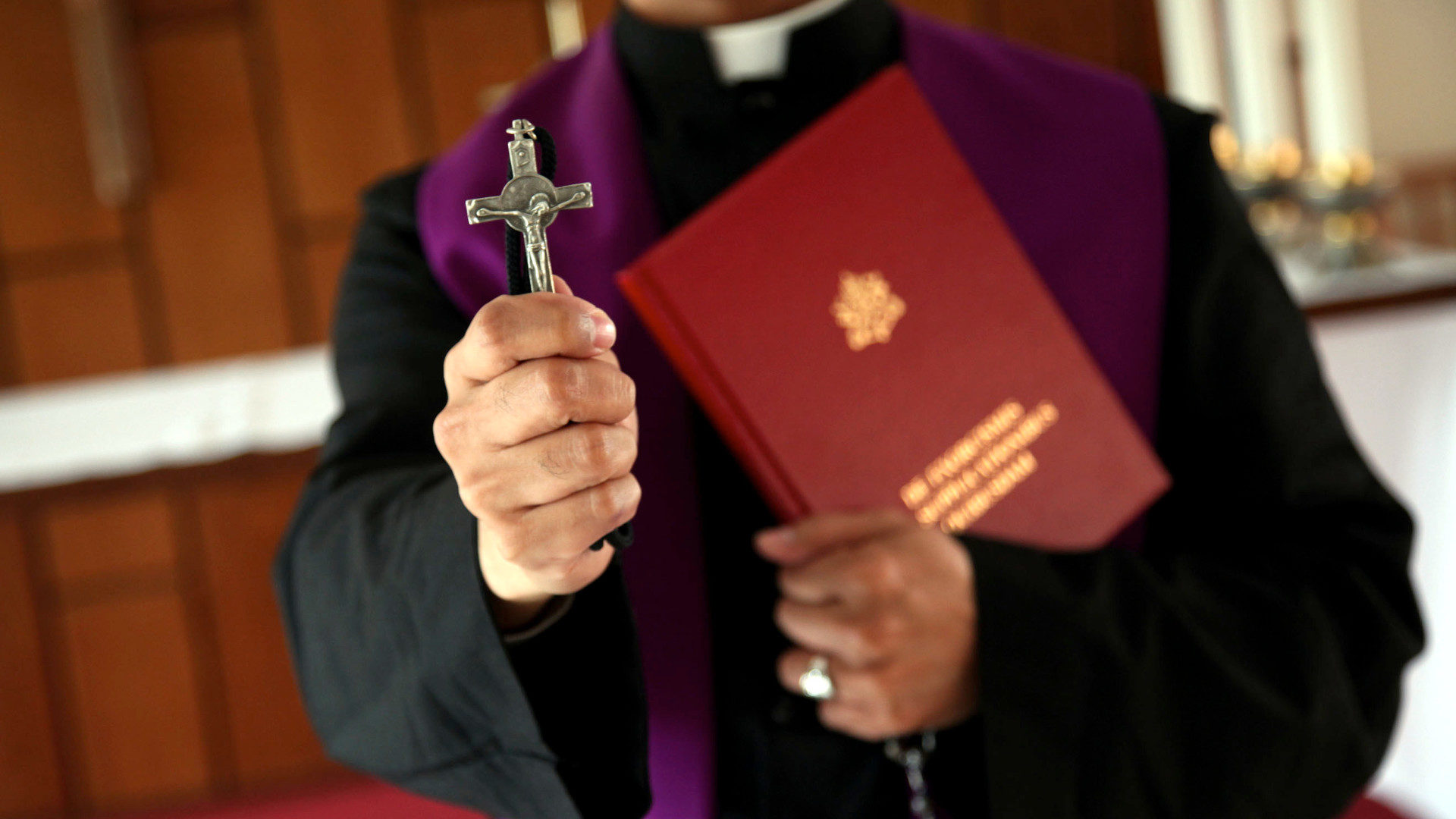 Ein Priester hält ein Kreuz in der Hand.