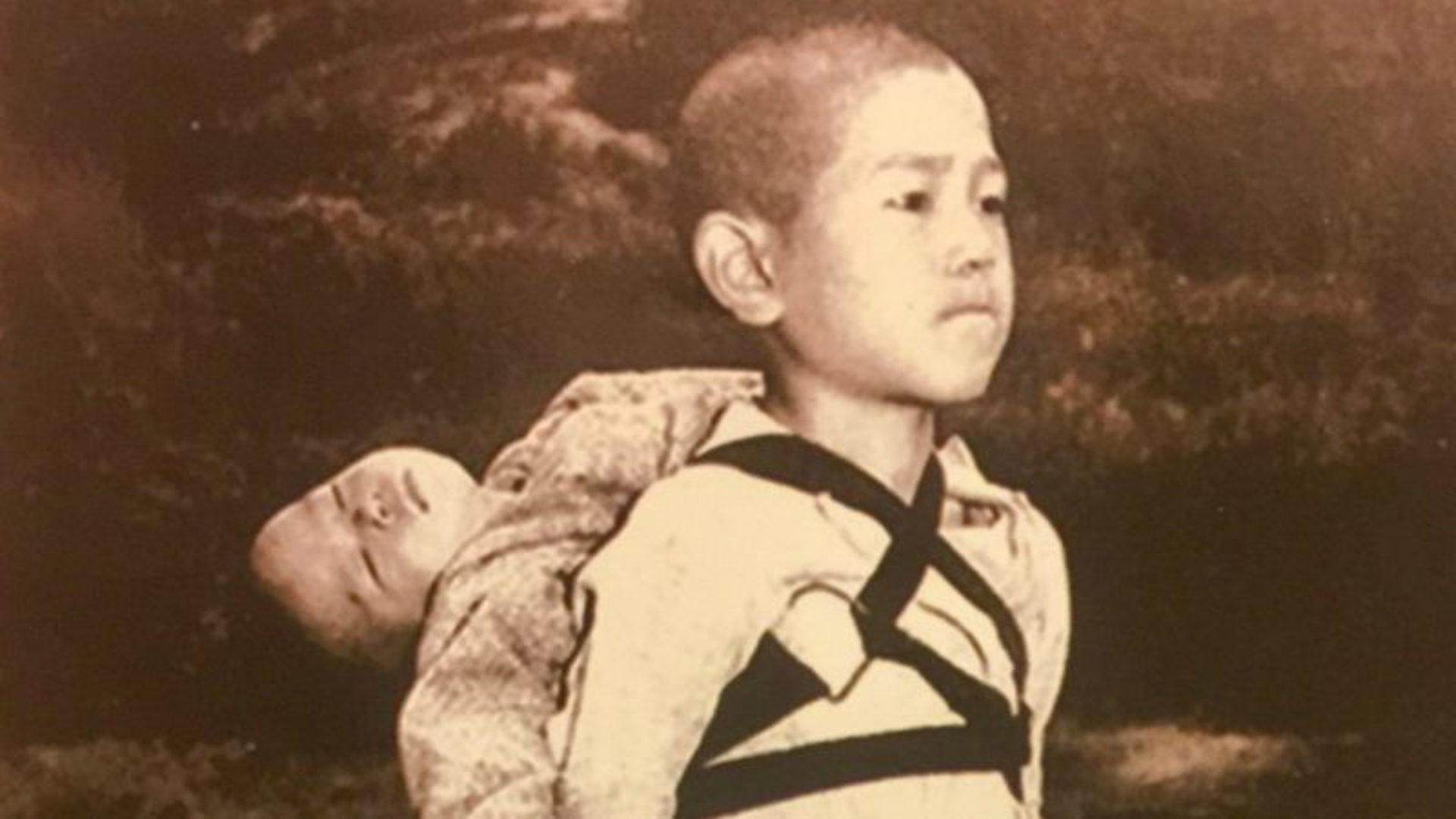Der Knabe von Nagasaki trägt seinen toten Bruder zur Leichenverbrennung.