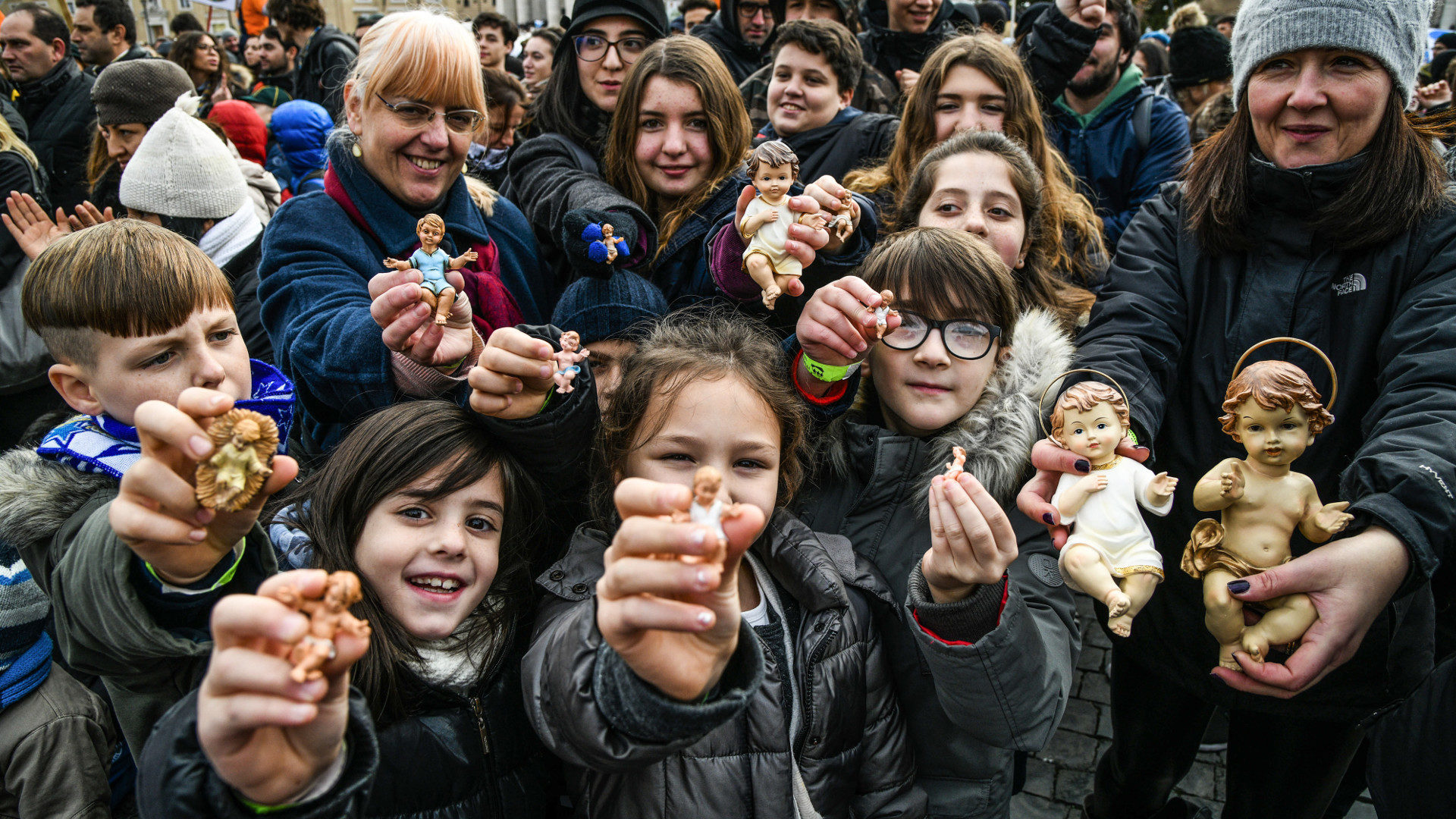 Religion macht fröhlich: Kinder und Erwachsene halten auf dem Petersplatz Figuren von Jesuskindern vor sich.