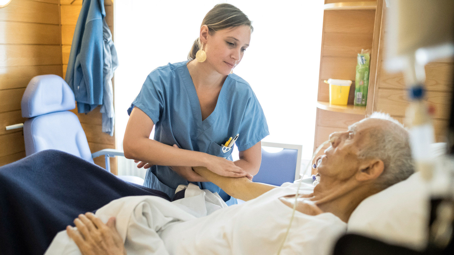 Eine Pflegerin massiert den Arm eines bettlägerigen Mannes in einer Palliativstation