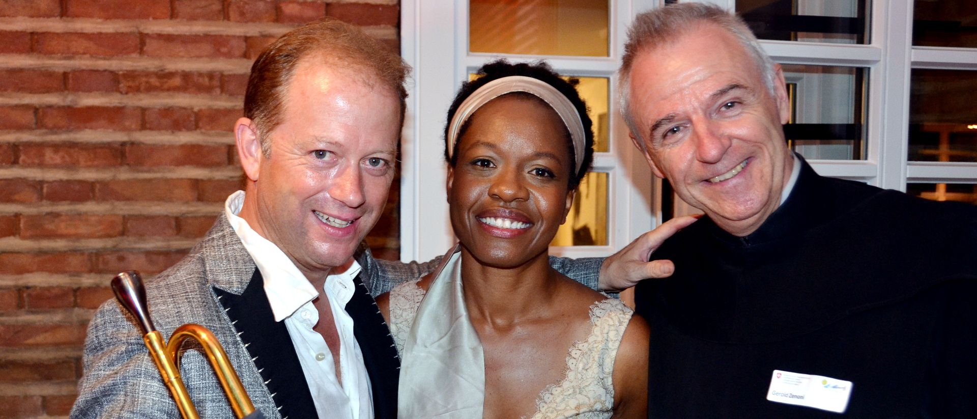 Bruder Gerold Zenoni (r.) mit dem Schweizer Startrompeter Dani Felber und einer Teilnehmerin am 1. August-Empfang 2018 in der Residenz des Schweizer Generalkonsuls in Frankfurt am Main  | ©&nbsp;zVg