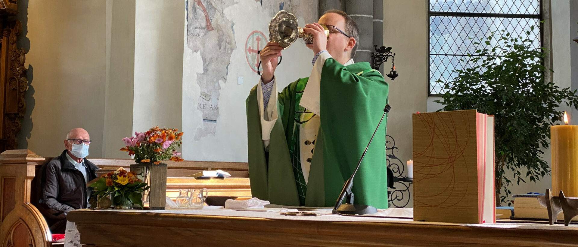 Pfarrer Daniel Noti trinkt das Blut Christi. Im Hintergrund ist der Sakristan mit Maske zu sehen.