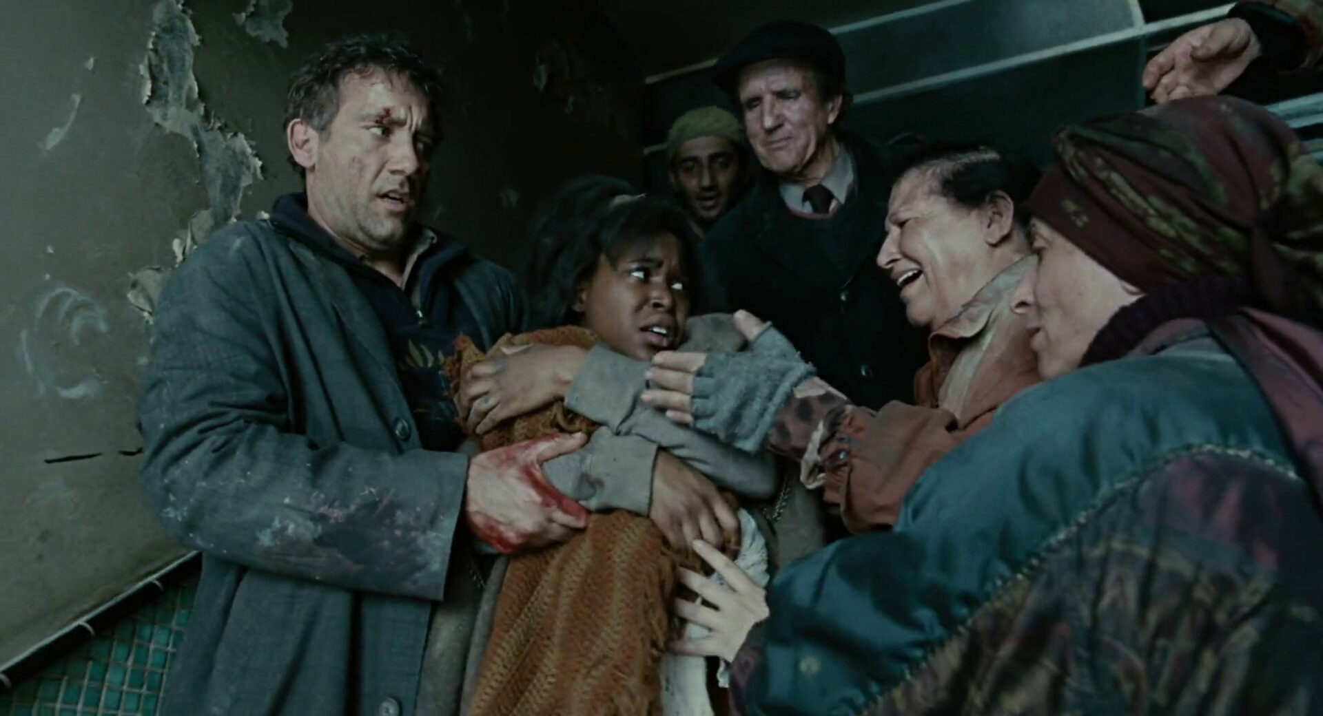 Theo (Clive Owen) bringt Kee (Claire-Hope Ashitey) und das Baby aus dem Haus. Die Menschen wollen das Wunder-Kind berühren. Screenshot.