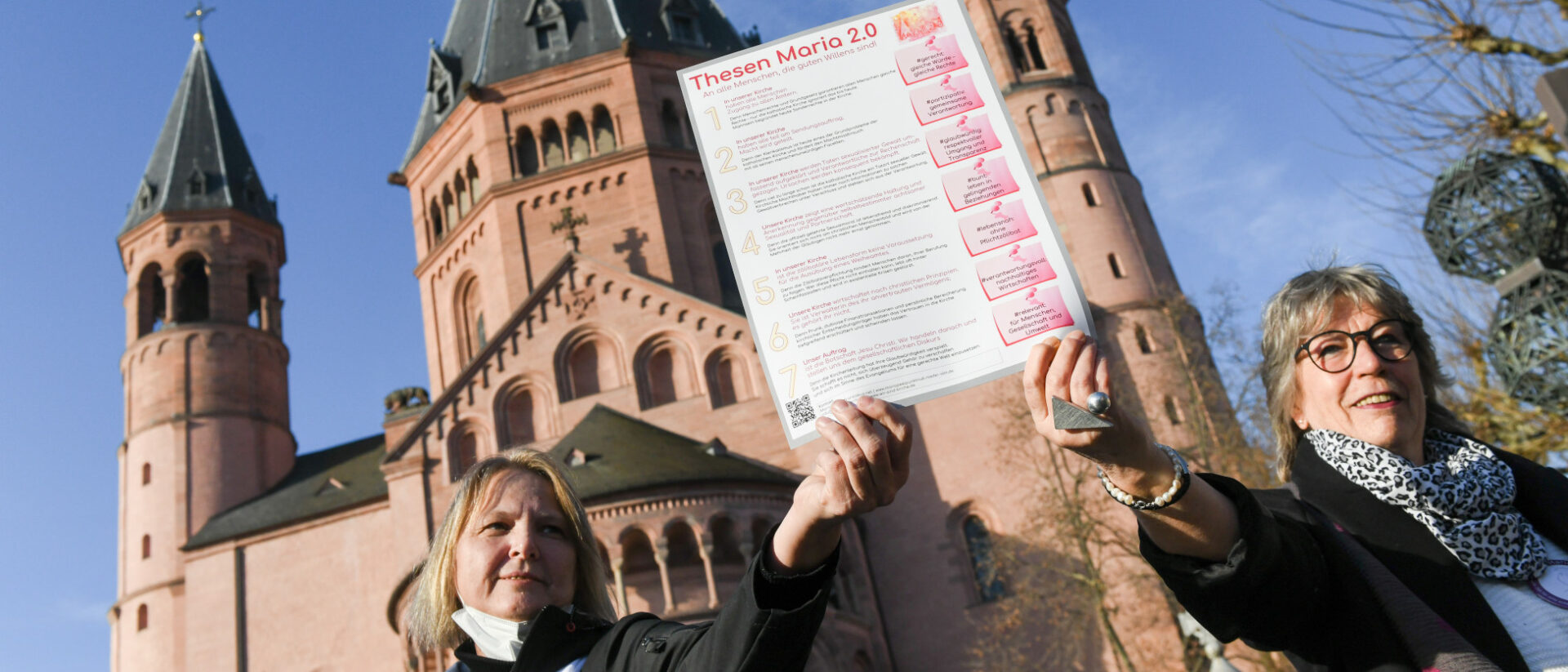 Andrea Keber (l.) und Beate Berdel-Mantz halten die Thesen der Initiative Maria 2.0 empor vor dem Thesenanschlag 2.0 am 21. Februar 2021 vor dem Dom in Mainz.