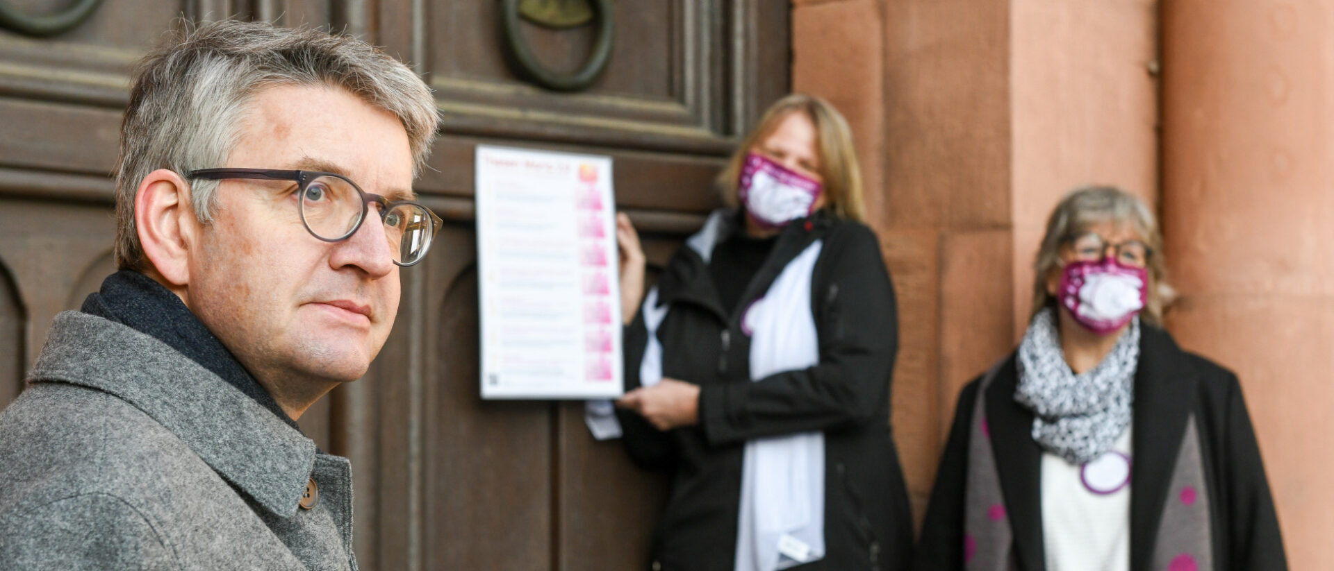 Peter Kohlgraf, Bischof von Mainz, steht neben zwei Frauen während des Thesenanschlags 2.0 der Initiative Maria 2.0.