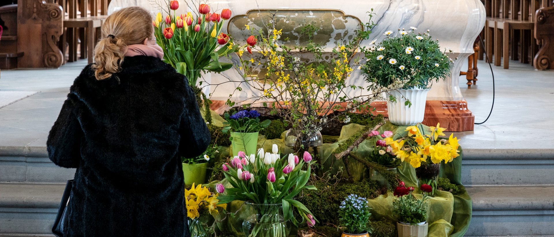 Eine Frau steht vor dem Blumengesteck für Hans Küng vor dem Altar in der Kirche.