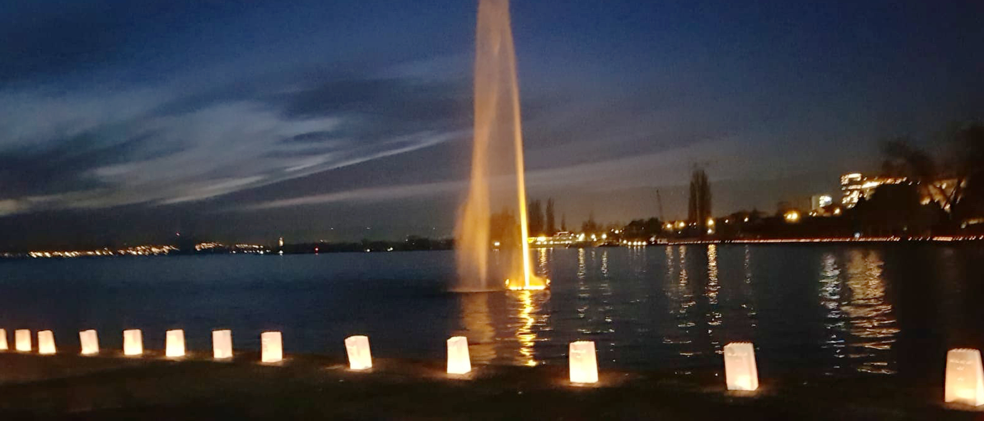 Lichttüten bilden eine Kette am Seeufer.