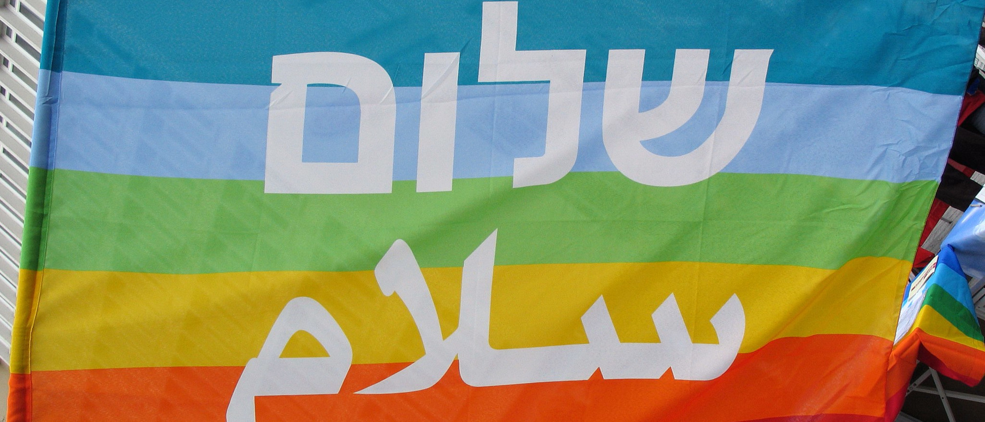 Regenbogenfahne mit der Aufschrift Shalom und Salām in hebräisch und arabisch