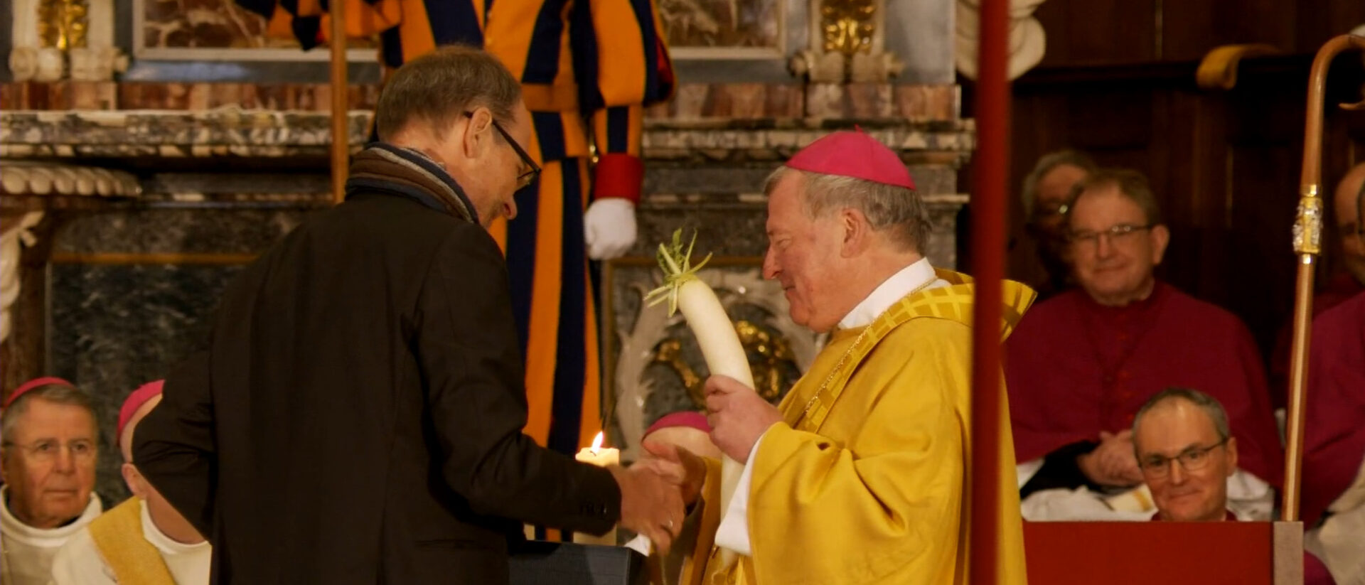 Luc Humbel überreicht dem neuen Weihbischof Josef Stübi eine Saftwurzel.