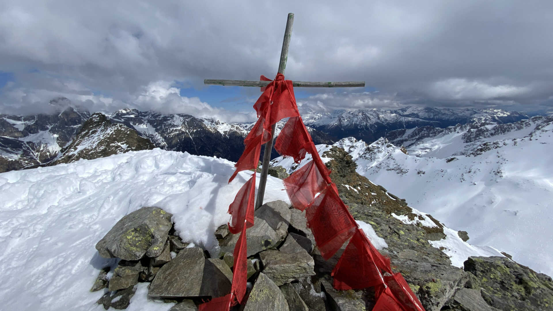 Tirol meets Tibet: Gipfelkreuz und tibetische Gebetsfahnen in den Alpen.