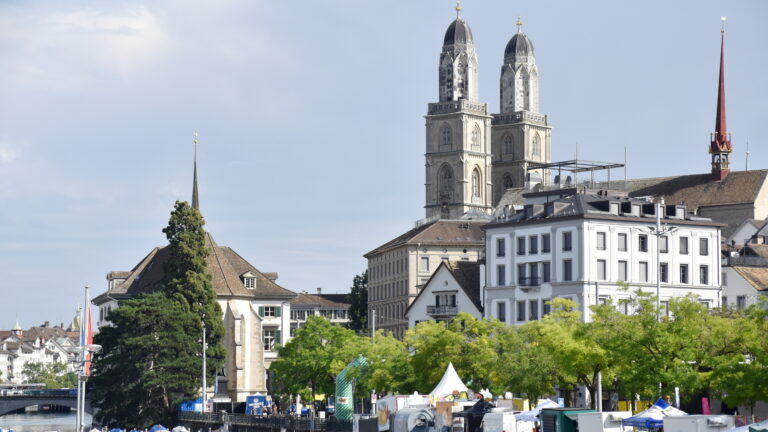 Blick auf Türme des Grossmünsters und der Wasserkirche in Zürich, versteckt hinter Bäumen an der Limmat. | Barbara Ludwig