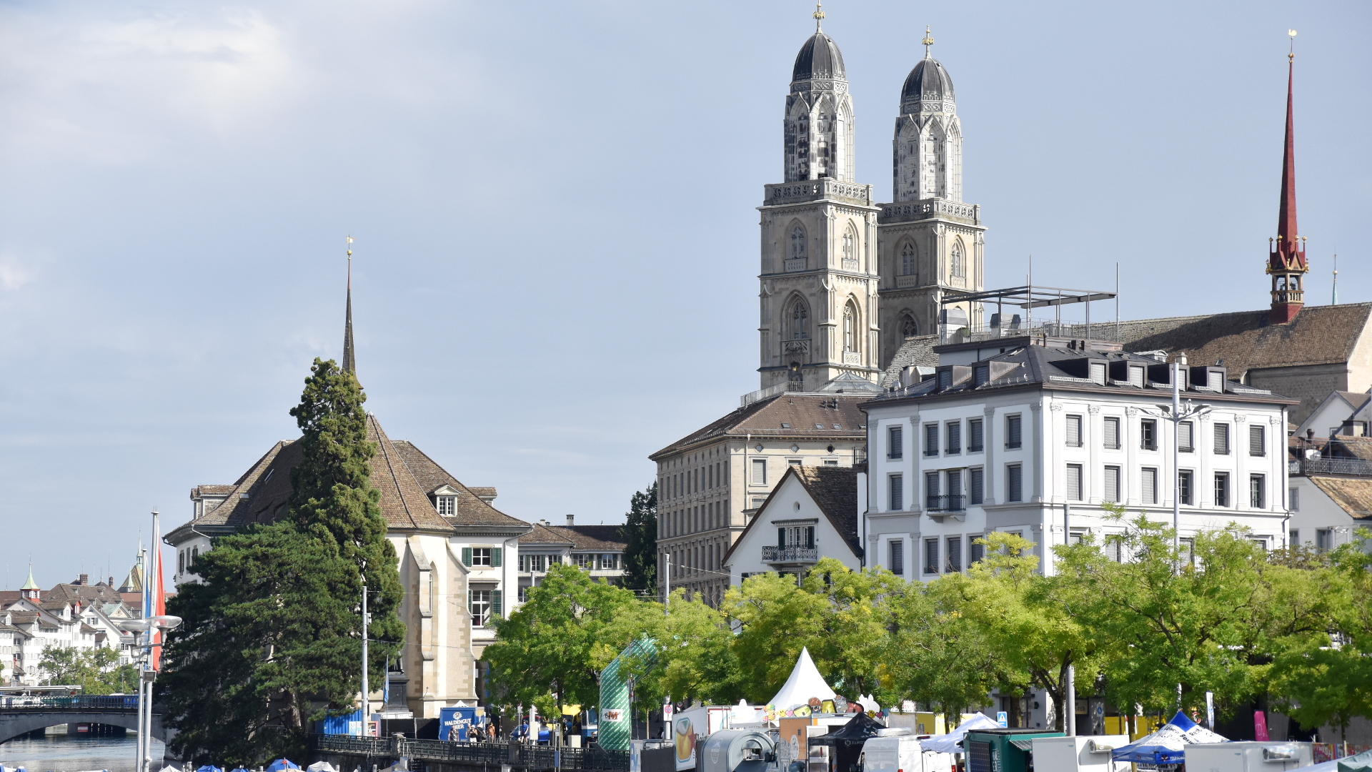 Blick auf Türme des Grossmünsters und der Wasserkirche in Zürich, versteckt hinter Bäumen an der Limmat.