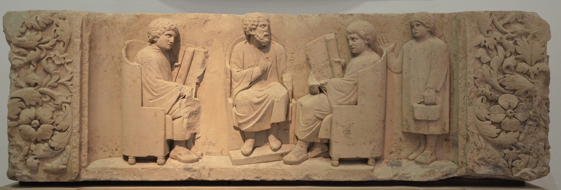 Schulstunde im antiken Rom: der Lehrer (wahrscheinlich ein Grieche) mit zwei Schülern am Lernen, der dritte kommt verspätet, 180–185 v. Chr. Trier, Rhein. Landesmuseum
