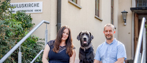 Ellen Weinmann und Florian Düsterwald sitzen mit ihrem Hund auf den Stufen vor der künftigen Tierbestattungskirche in Albstadt. | Ramona Balm/Fotostudio Bossenmaier/KNA