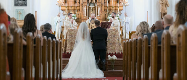 Ein Hochzeitspaar kniet vor dem Altar während der Priester die Wandlung vollzieht.