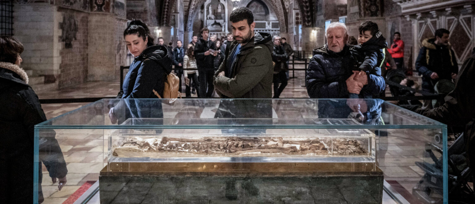 Menschen gehen am Glasreliquiar vorbei, in dem die Gebeine des heiligen Franziskus von Assisi in der Unterkirche der Basilika San Francesco in Assisi (Italien) ausgestellt sind. | KNA