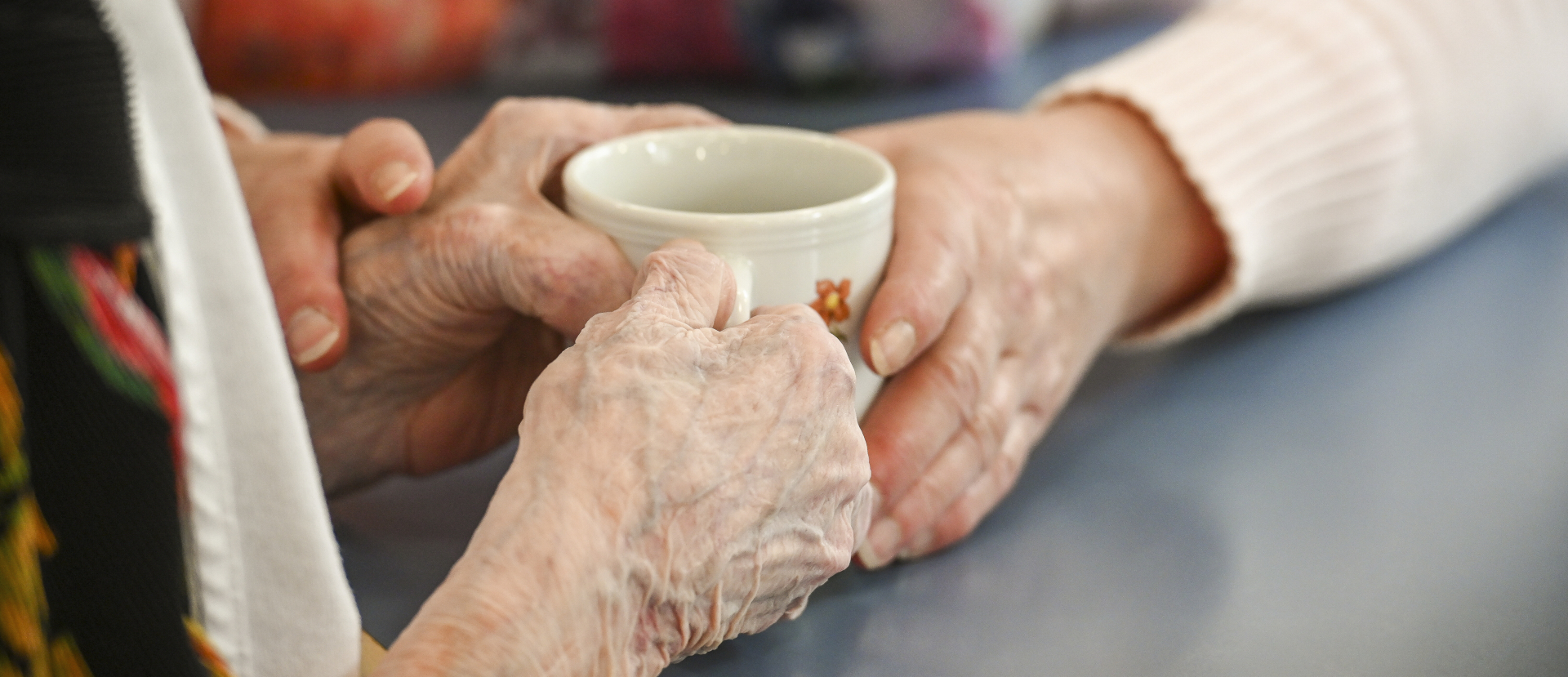 Unterstützung bei alltäglichen Handlungen: Eine Betreuerin in einem Altersheim hilft einer blinden Frau mit der Kaffeetasse.